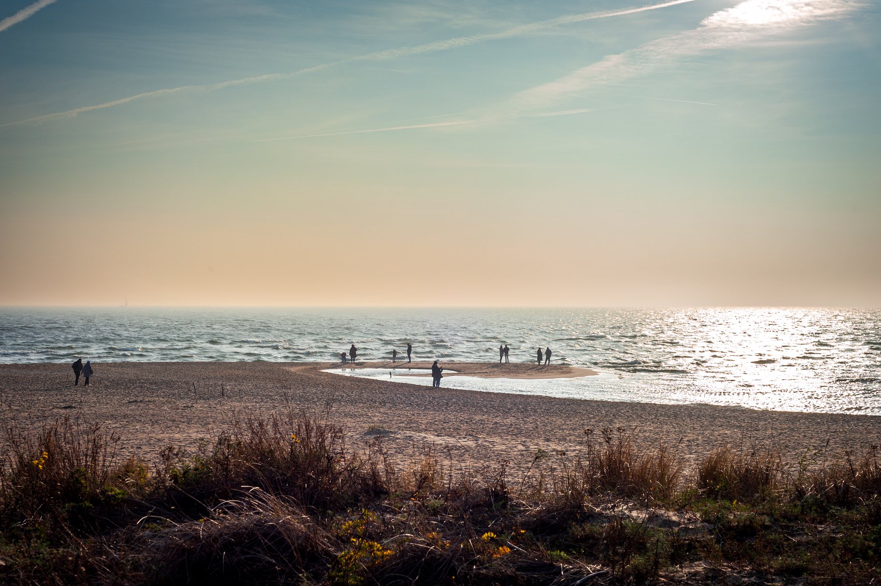 People walking along a broad beach in Hel as low autumn sun sparkles across the Baltic Sea.
