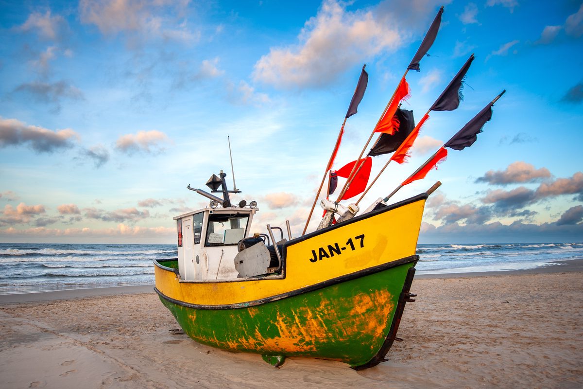 Bright yellow and green fishing boat Jantar 17 resting on a snow-dusted winter beach.