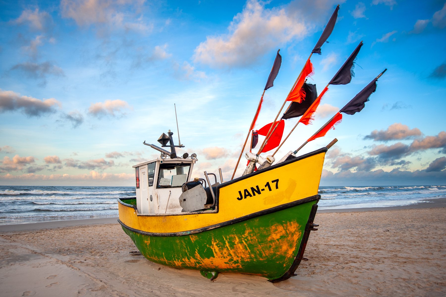 Bright yellow and green fishing boat Jantar 7 resting on a snow-dusted winter beach.