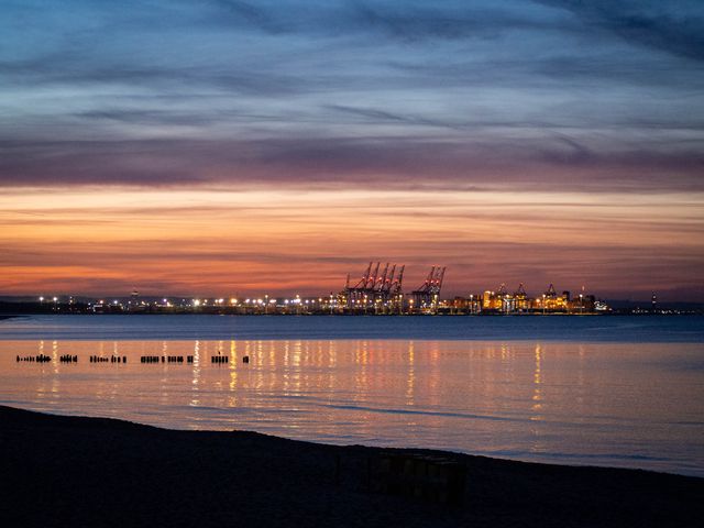 Distant cranes of Gdańsk port silhouetted across calm water under a pink and violet dusk sky.