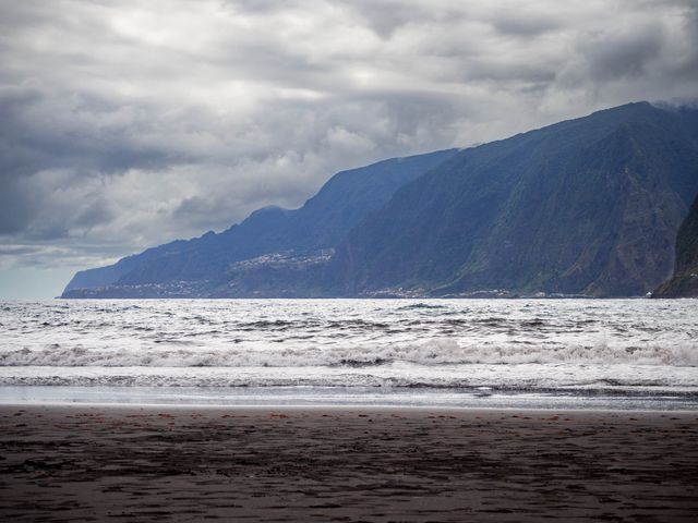 White Atlantic surf crossing the black sand of Seixal Beach below Madeira's steep green mountains.