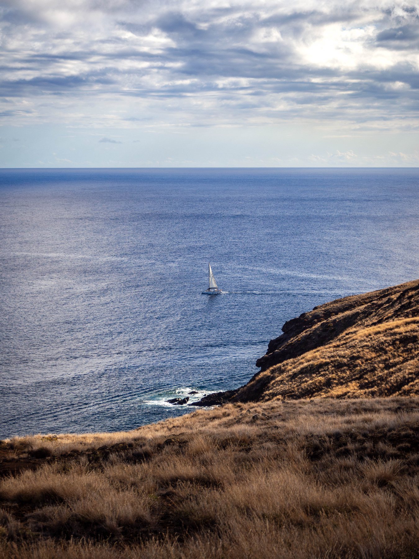 A lone sailboat on deep blue water beside the dry ochre slopes of São Lourenço.