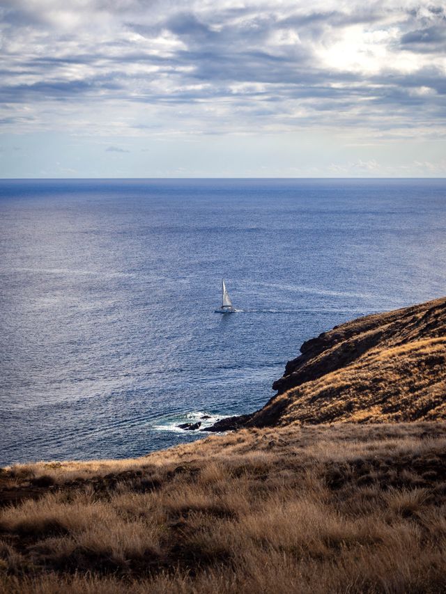 A lone sailboat on deep blue water beside the dry ochre slopes of São Lourenço.