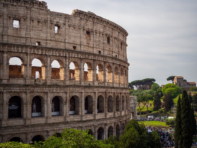 The weathered arcades of the Colosseum seen above spring-green trees in Rome.