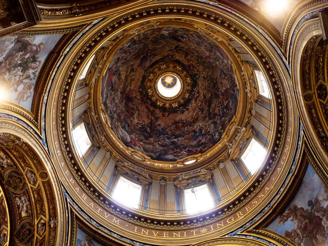 Looking straight up into an ornate gilded church dome filled with painted figures in Rome.