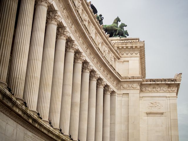 Close upward view along a monumental row of pale stone columns and carved entablature in Rome.