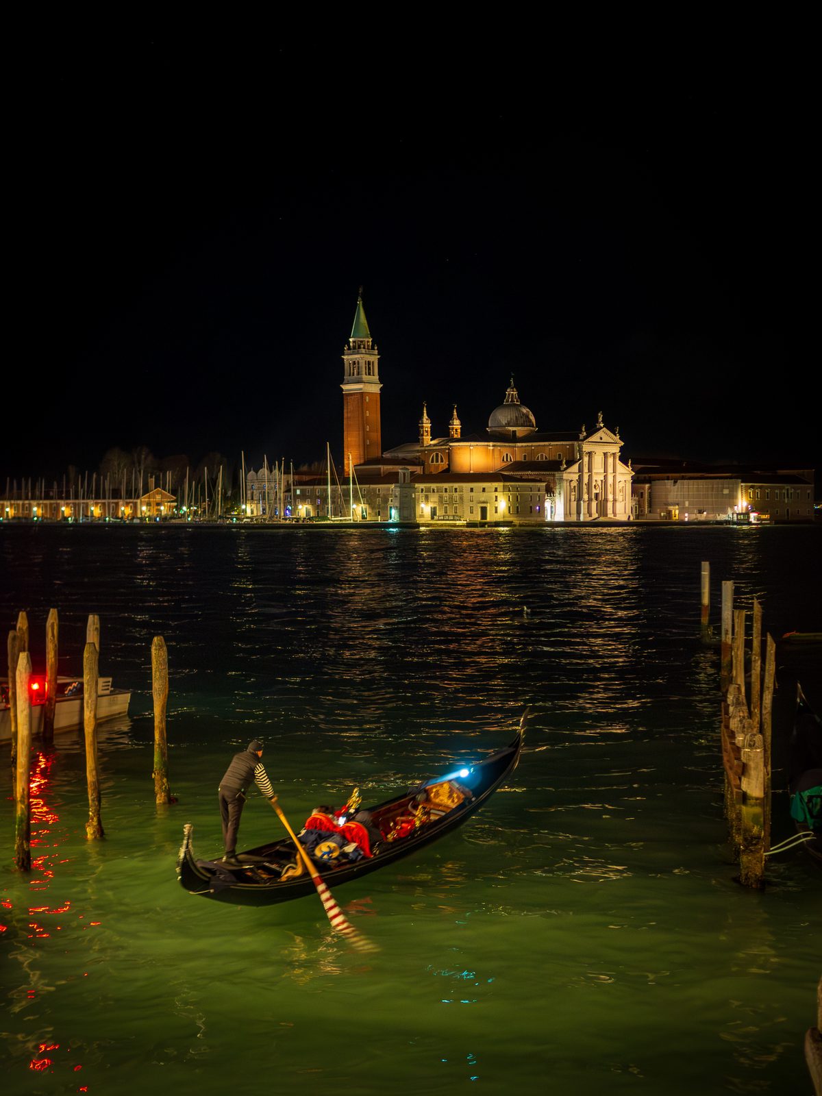 A gondola crossing dark lagoon water with illuminated San Giorgio Maggiore in the distance.