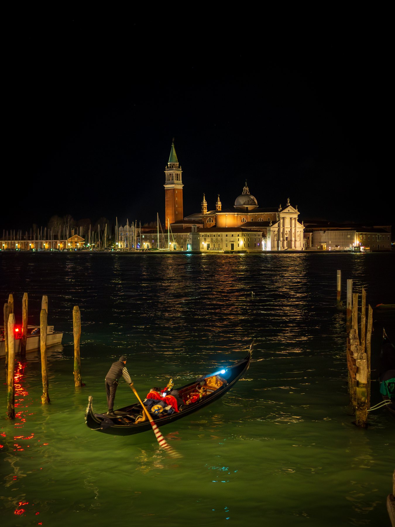A gondola crossing dark lagoon water with illuminated San Giorgio Maggiore in the distance.