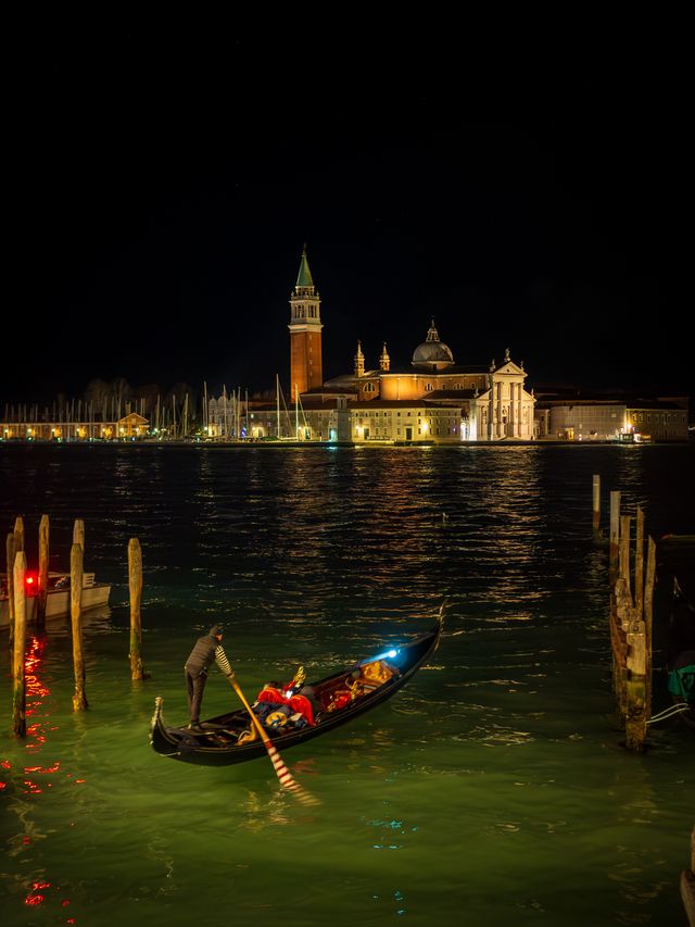 A gondola crossing dark lagoon water with illuminated San Giorgio Maggiore in the distance.
