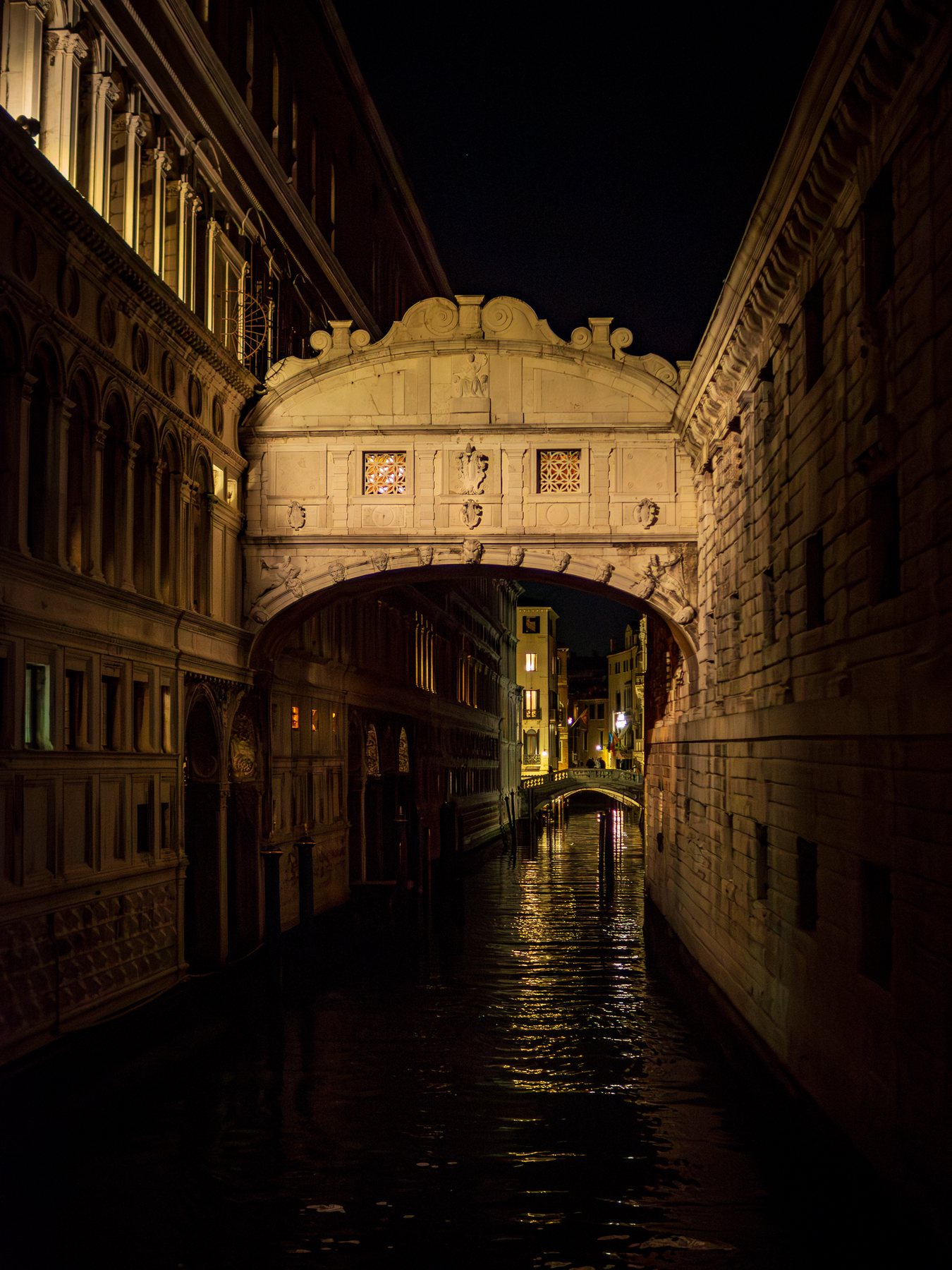 The enclosed Bridge of Sighs glowing above a narrow black canal between shadowed palaces.