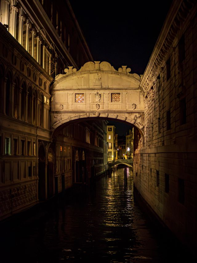 The enclosed Bridge of Sighs glowing above a narrow black canal between shadowed palaces.