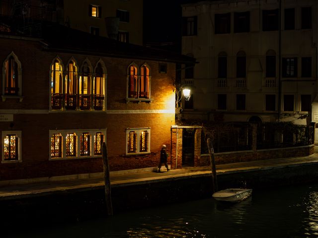 Rows of amber-lit Gothic windows reflected in a quiet Venetian canal at night.