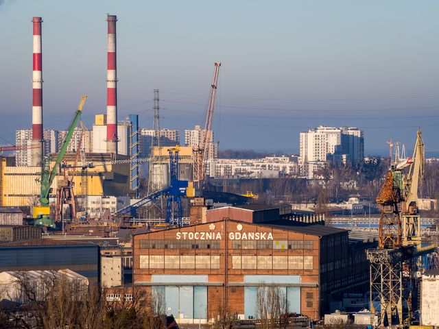 Shipyard cranes, striped chimneys, and the historic Stocznia Gdańska workshop in clear winter light.