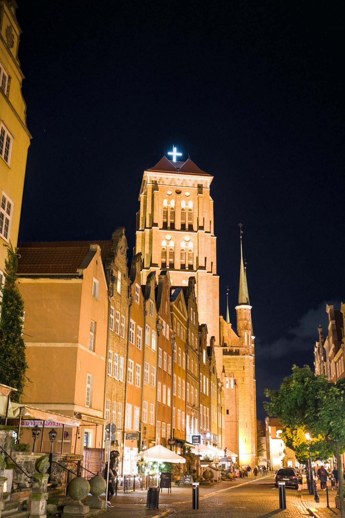 The warmly illuminated tower of St Catherine's Church rising over a Gdańsk street at night.