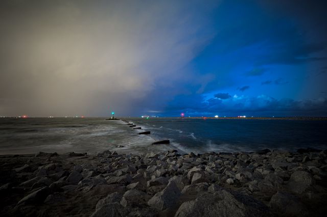 Long-exposure blue storm light above a rocky Baltic shore, with navigation lights along the horizon.