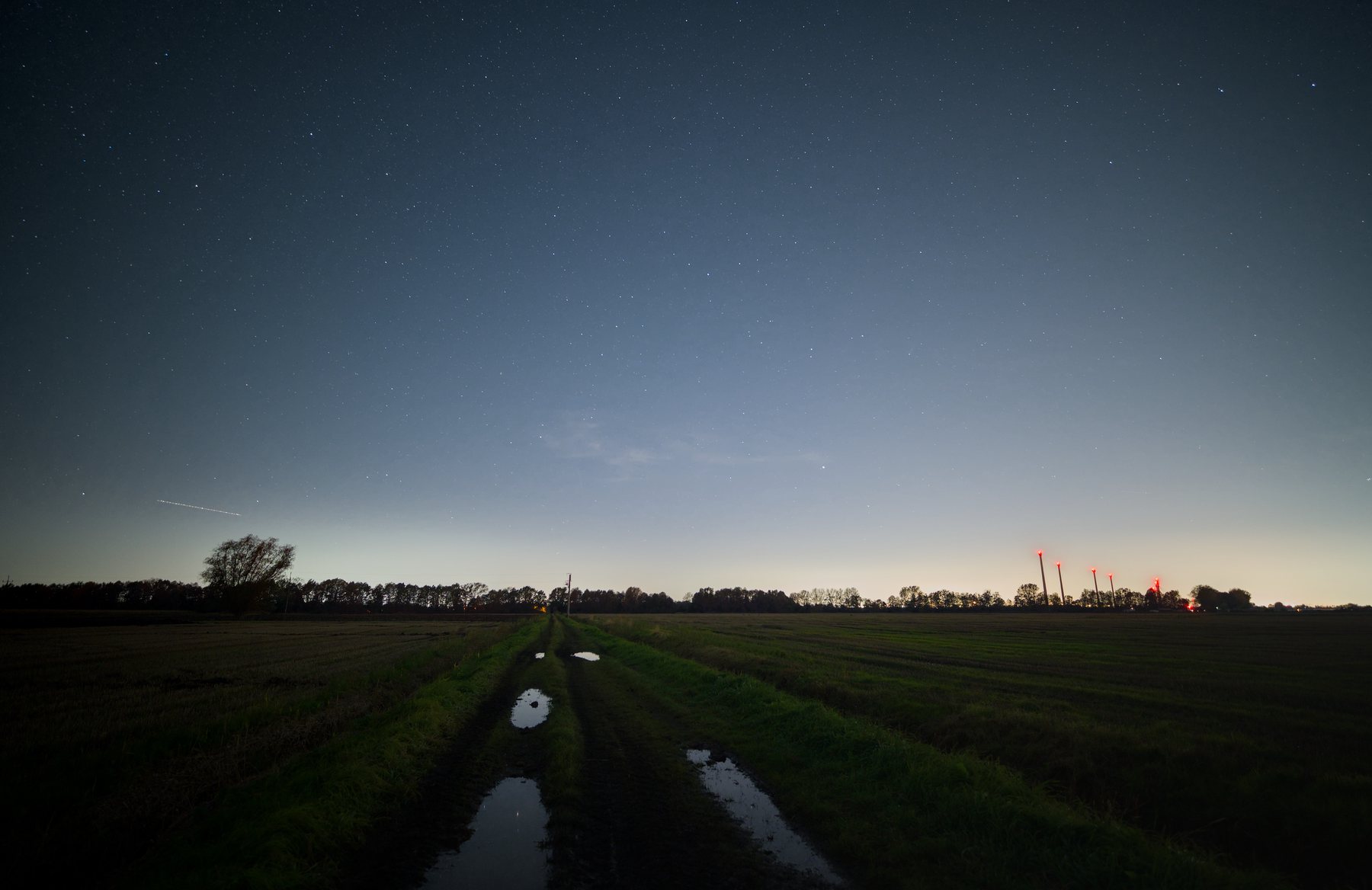 A wet track crossing dark autumn fields beneath a faintly starred sky outside Gdańsk.