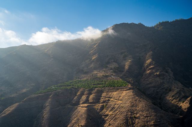 Terraced volcanic ridges and deep ravines on La Palma catching slanted light beneath low cloud.
