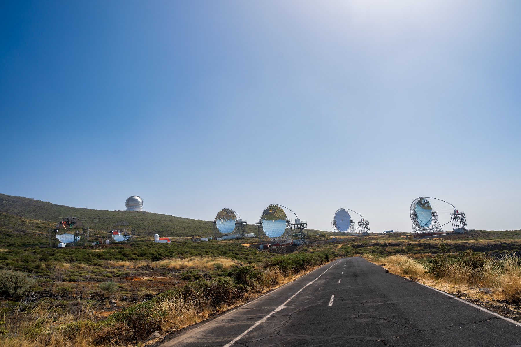 An empty mountain road approaching telescope domes and dishes at Roque de los Muchachos.