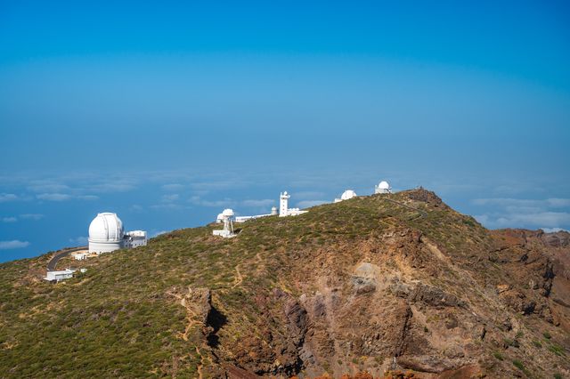 White observatory domes spaced along a steep volcanic ridge above the Atlantic cloud layer.