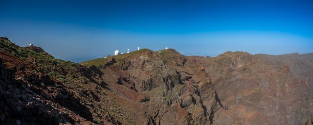 Panoramic volcanic ridge with distant telescope domes under a deep blue sky.