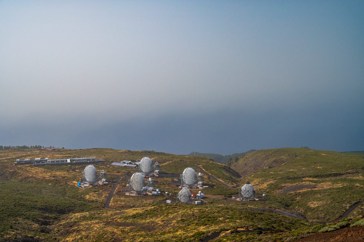 A cluster of small white telescope enclosures on a high plateau disappearing into thick cloud.