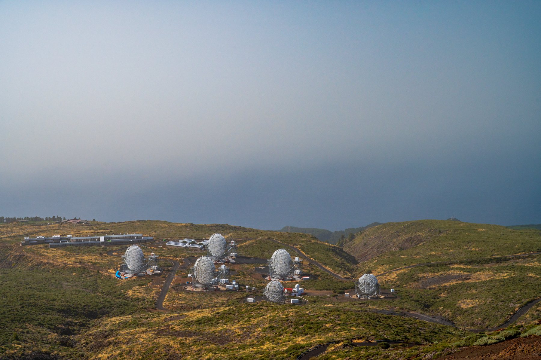 A cluster of small white telescope enclosures on a high plateau disappearing into thick cloud.