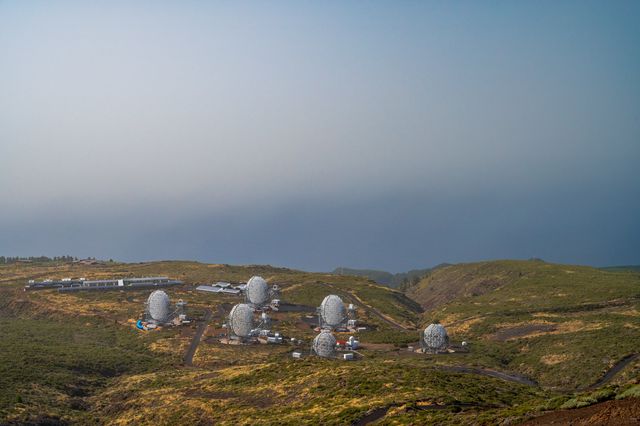 A cluster of small white telescope enclosures on a high plateau disappearing into thick cloud.