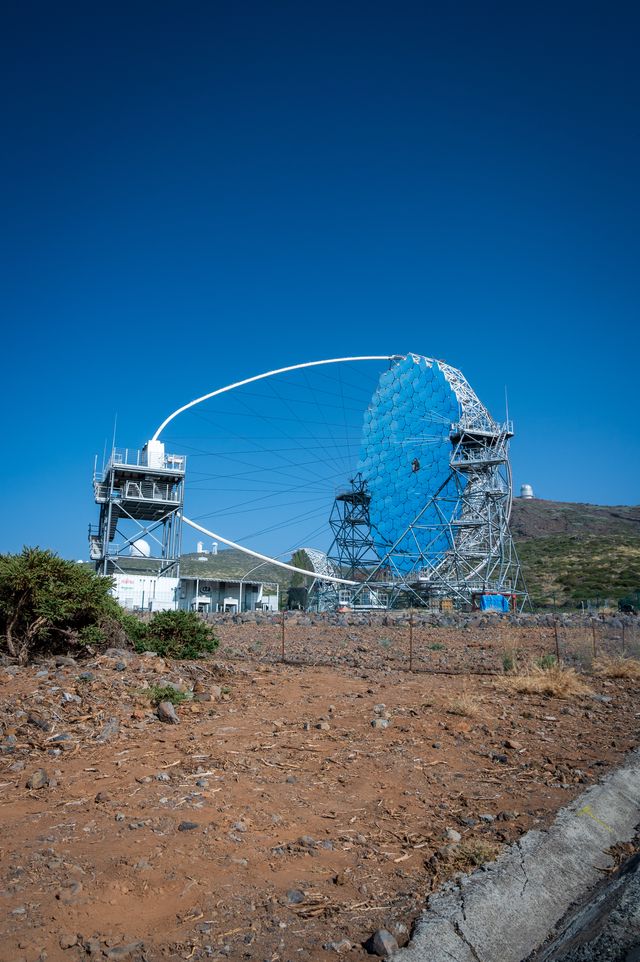 The exposed blue framework and segmented mirrors of a large telescope against clear sky.