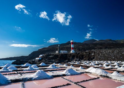 Fuencaliente lighthouse beyond white salt mounds and pink evaporation ponds beside the ocean.