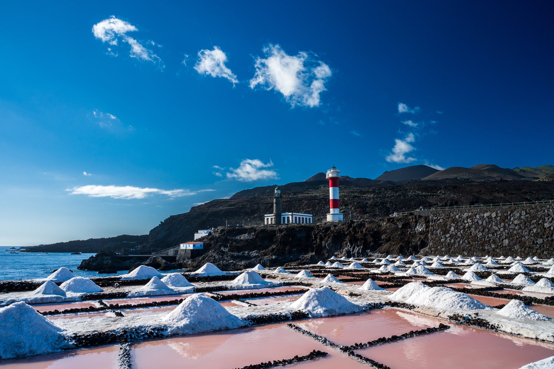 Fuencaliente lighthouse beyond white salt mounds and pink evaporation ponds beside the ocean.