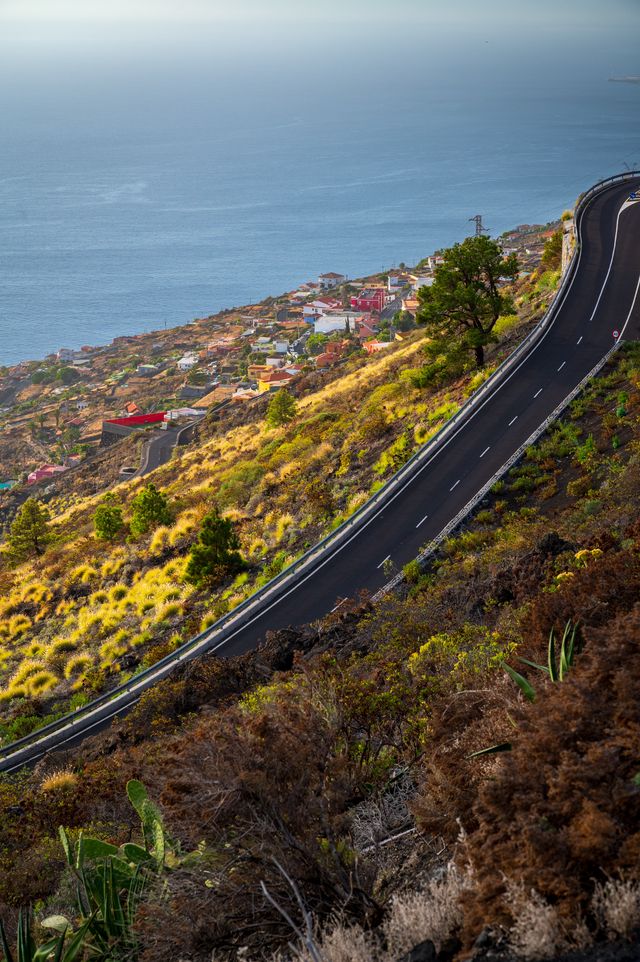 A narrow road winding sharply across a steep volcanic coastal slope on La Palma.