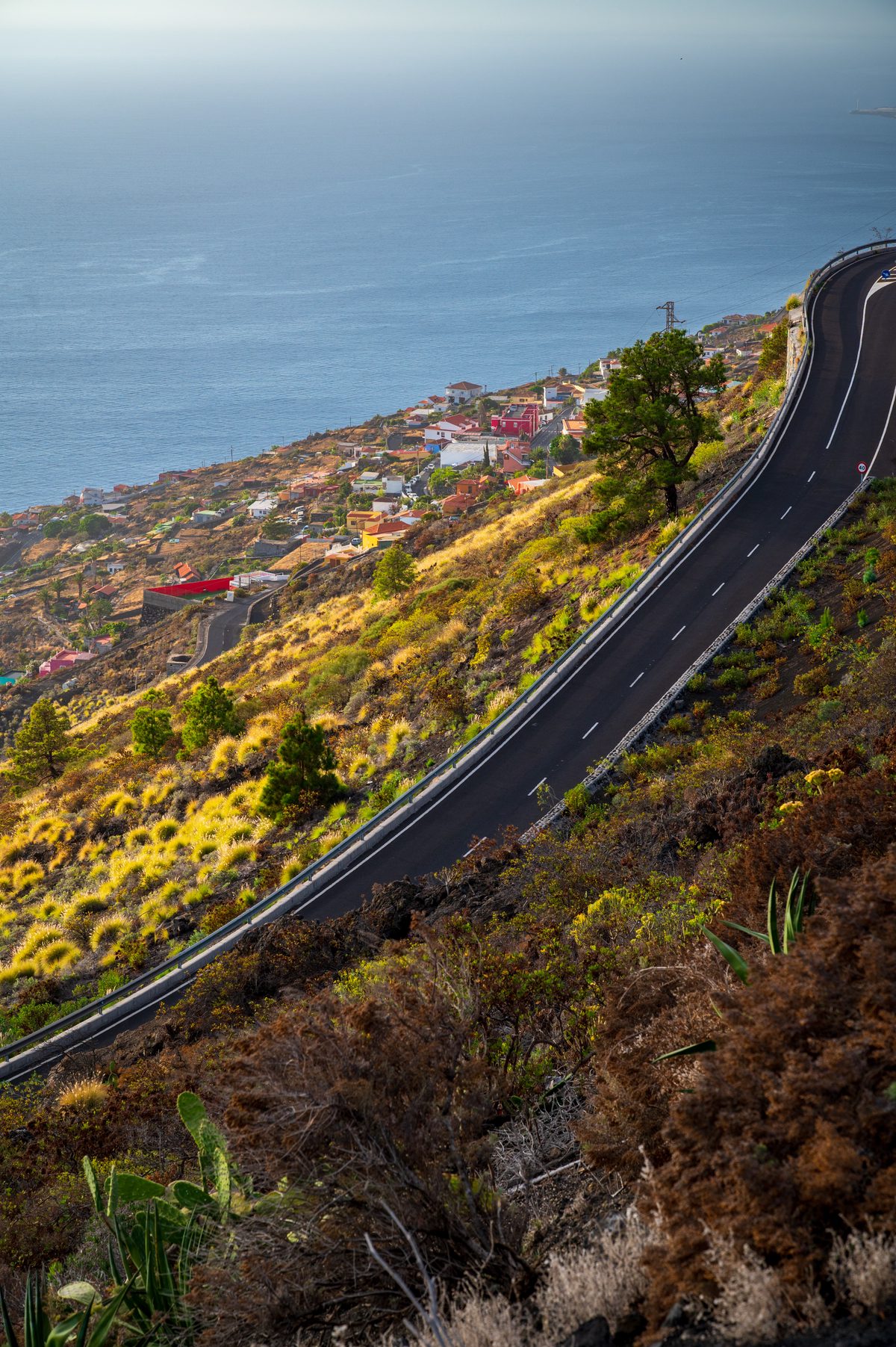 A narrow road winding sharply across a steep volcanic coastal slope on La Palma.