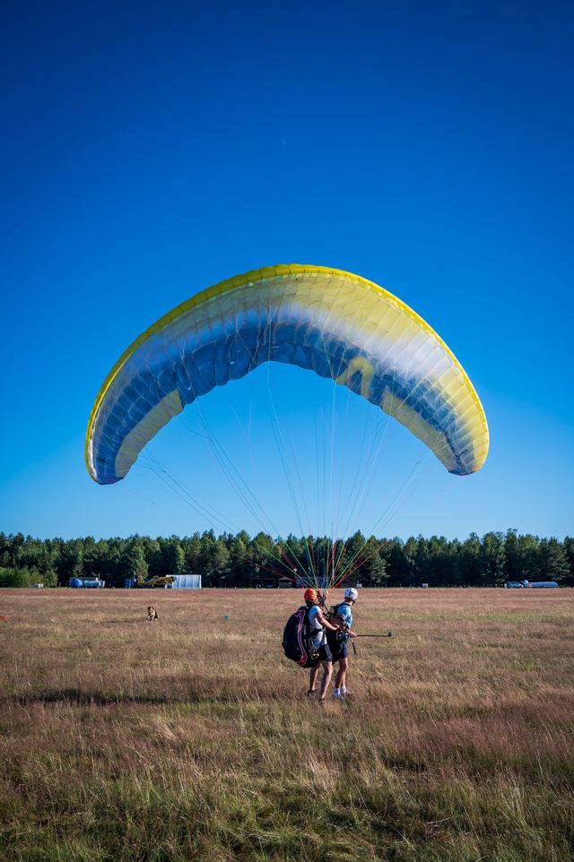 A pilot running beneath an inflated yellow and blue paraglider canopy on Borsk airfield.