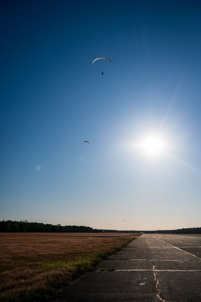 Two small paragliders circling near the sun above the long concrete runway.