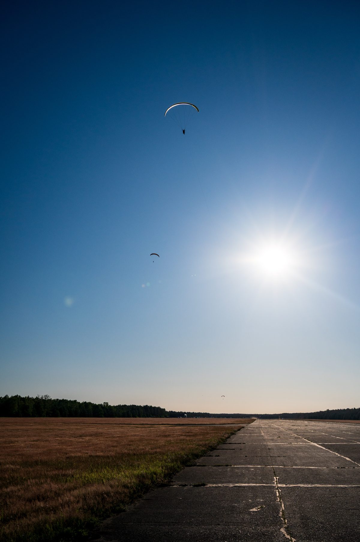 Two small paragliders circling near the sun above the long concrete runway.