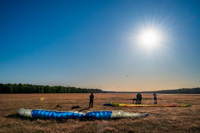 Pilots gathering around collapsed blue and yellow canopies in late-afternoon light.