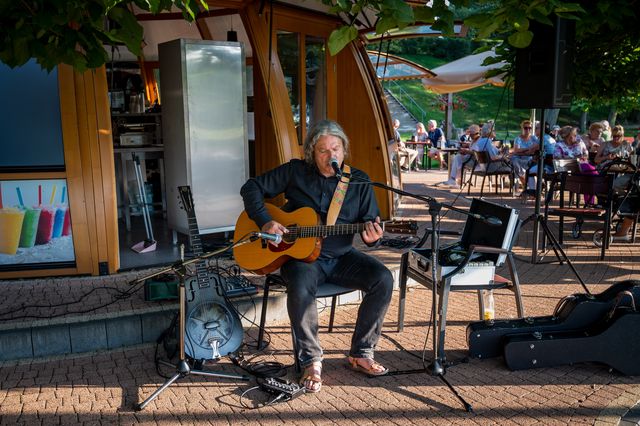 Paweł Szymański singing and playing acoustic guitar on an intimate park stage.