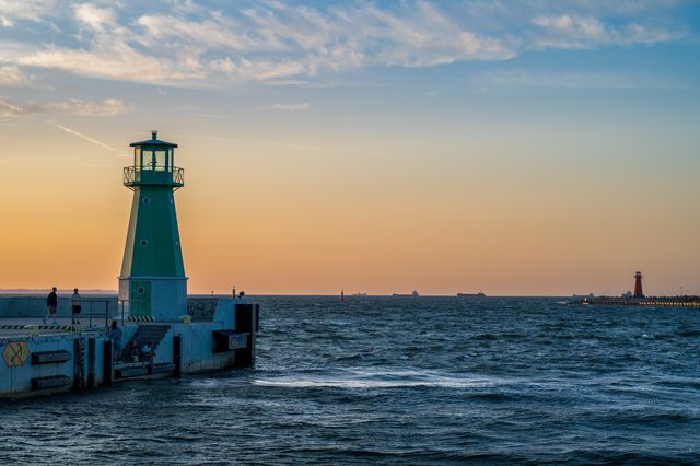 A green harbour light at the end of a pier with a red beacon across choppy water.