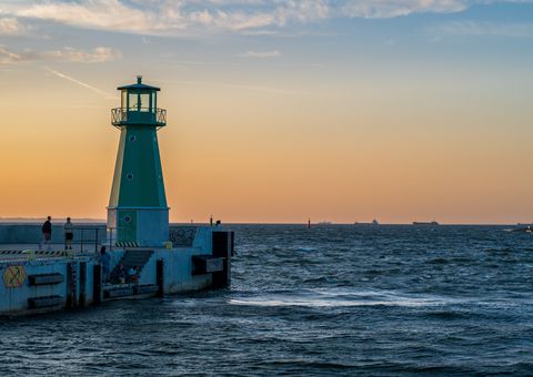 A green harbour light at the end of a pier with a red beacon across choppy water.