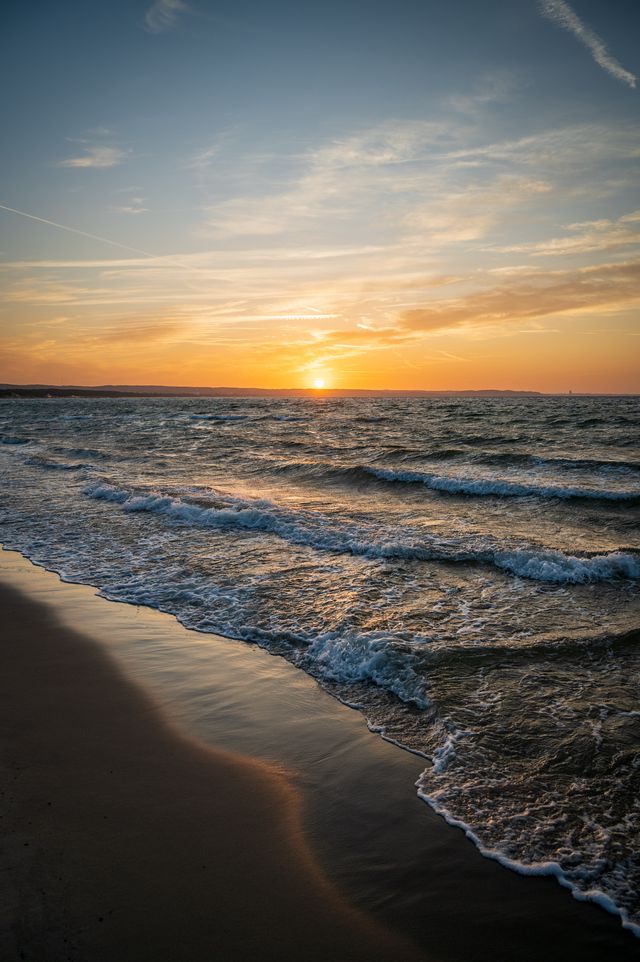 Small sunset waves folding onto smooth dark sand along the Gdańsk coast.