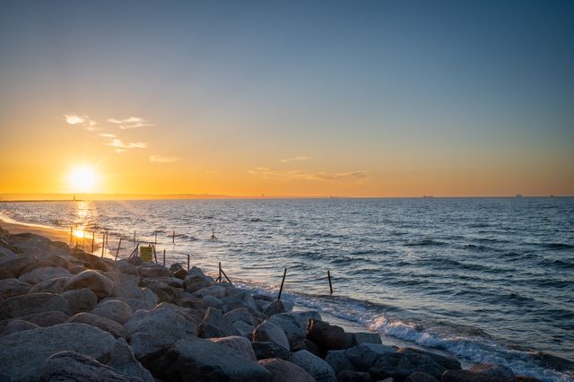 Golden sunset reflected between pale rocks on a long Baltic breakwater.