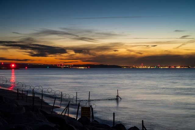 Red navigation light reflected in calm harbour water under a layered twilight sky.