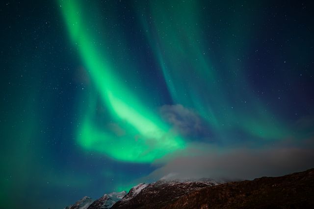 Vibrant green aurora borealis dancing across a starlit sky above a snow-capped mountain landscape in the Arctic night.
