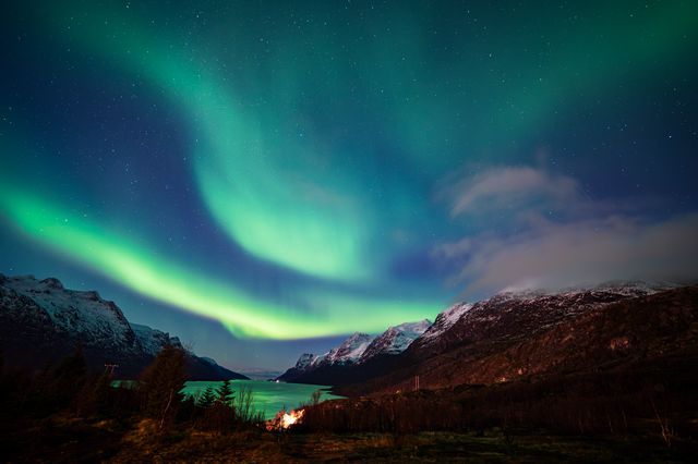 Vibrant aurora borealis dancing across the night sky above snow-capped mountains and a serene alpine lake, creating an ethereal green glow.