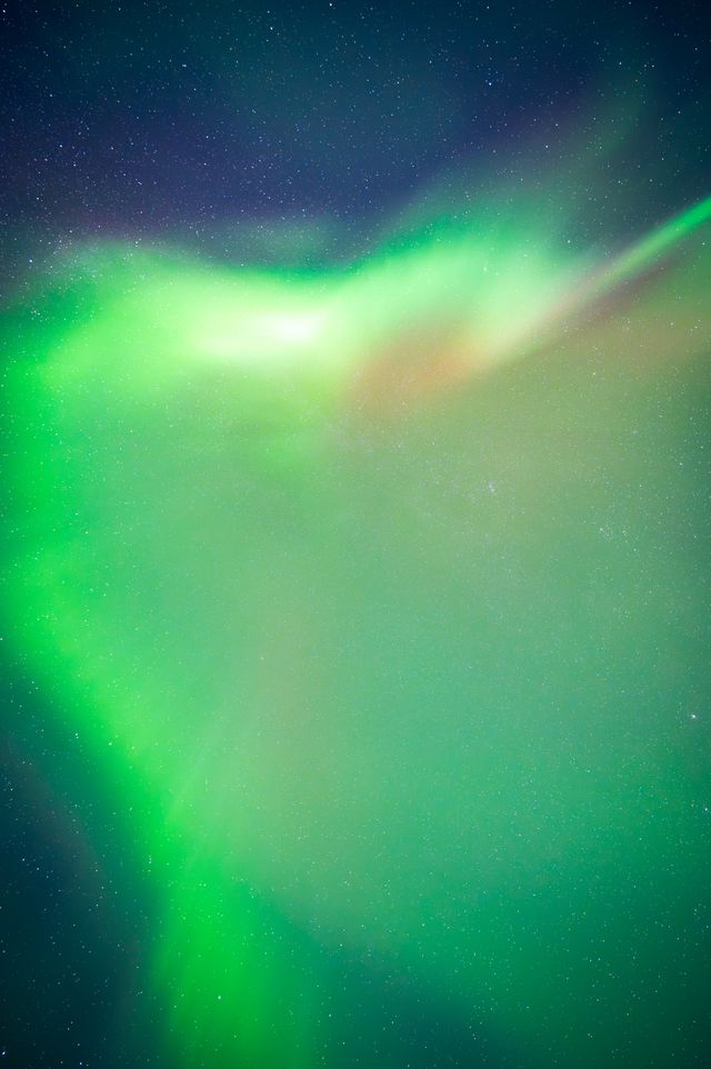 Vibrant aurora borealis with luminous green waves dancing across a starlit night sky, creating an ethereal natural light display.