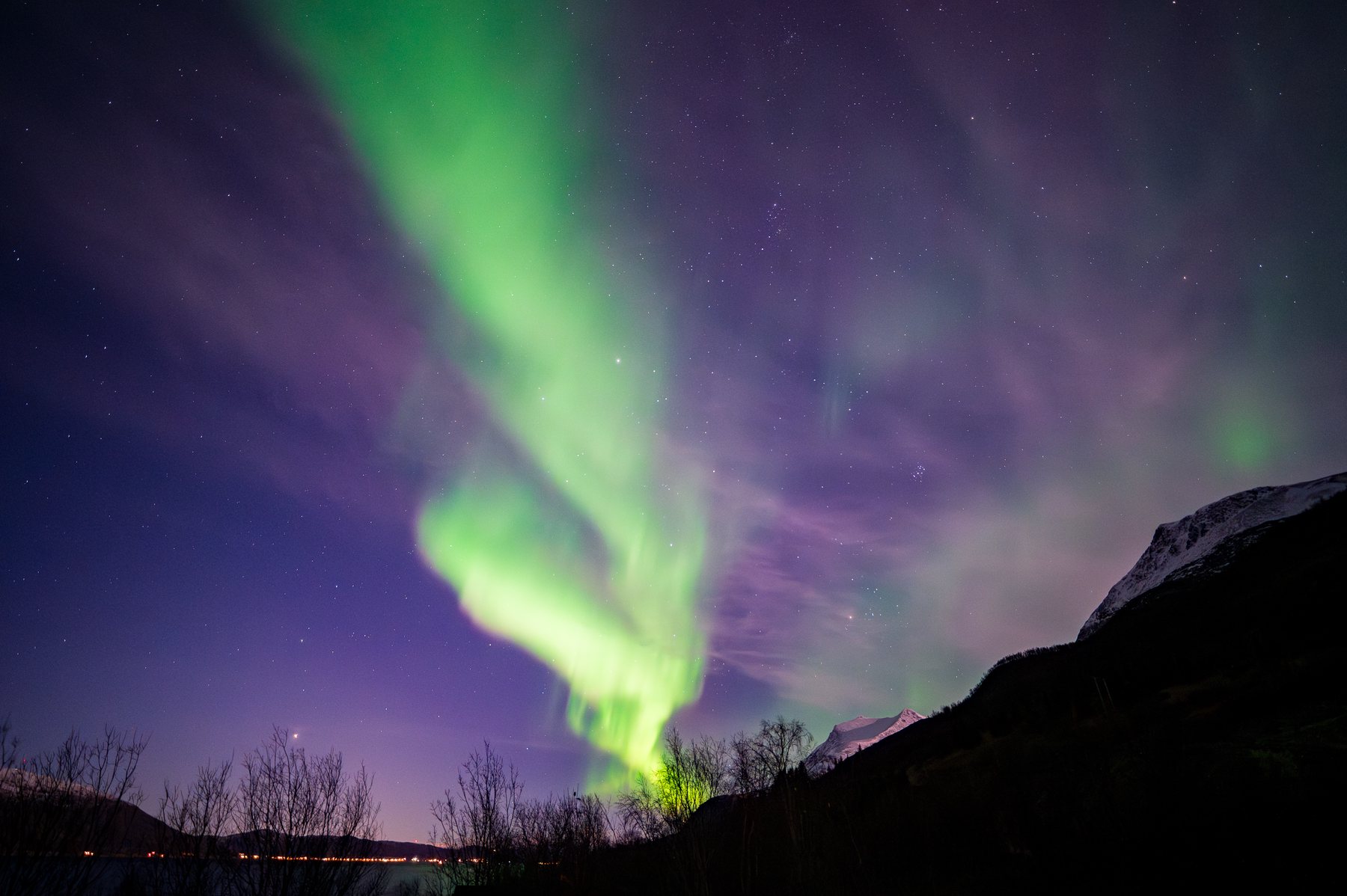 A twisting green aurora column framed by steep dark mountain slopes at Håkøybotn.