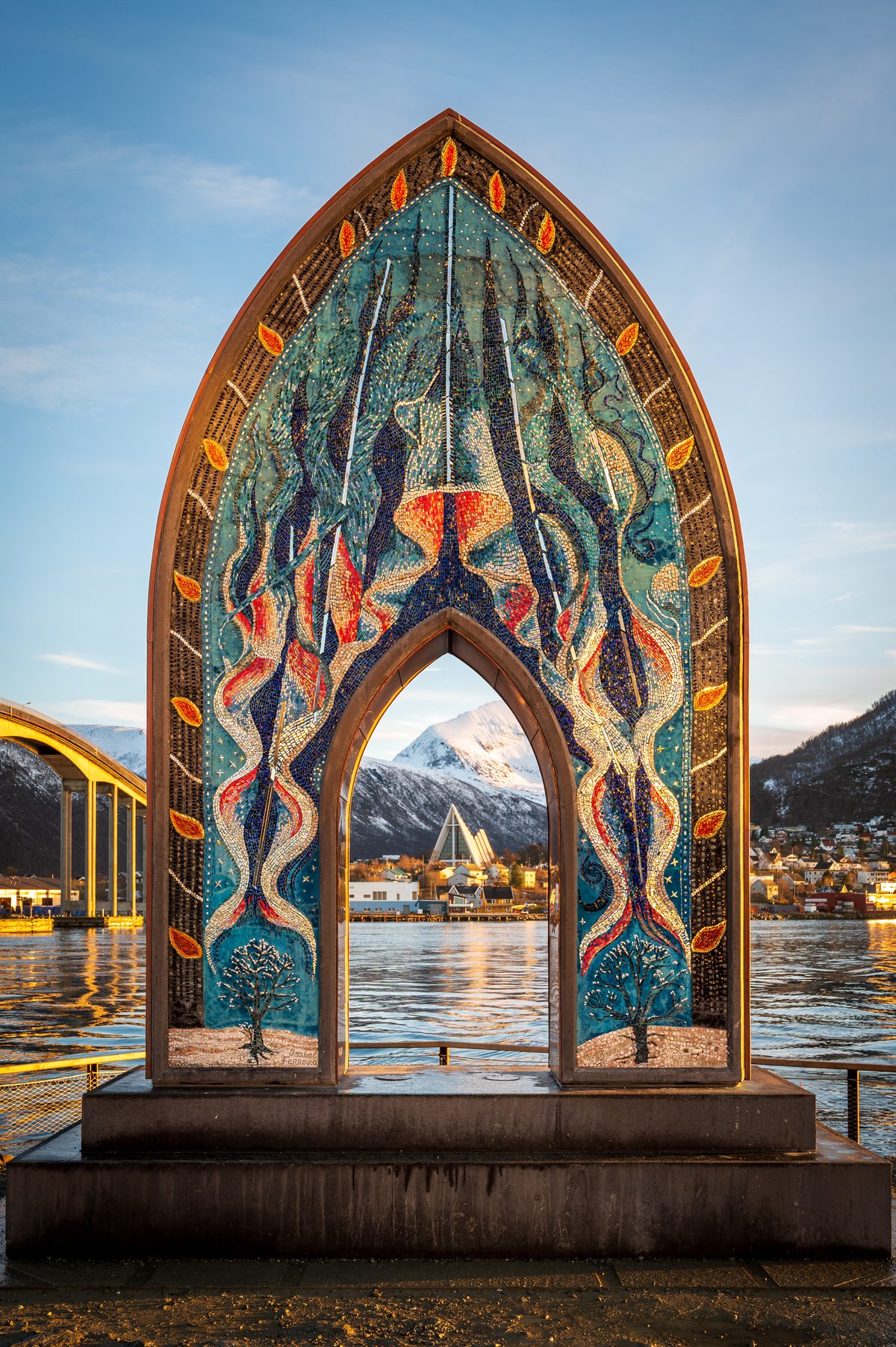 A colourful mosaic arch on Tromsø’s waterfront perfectly frames the Arctic Cathedral and snow-covered mountain beyond. The composition brings together public art, architecture and the dramatic landscape surrounding the Norwegian Arctic city.