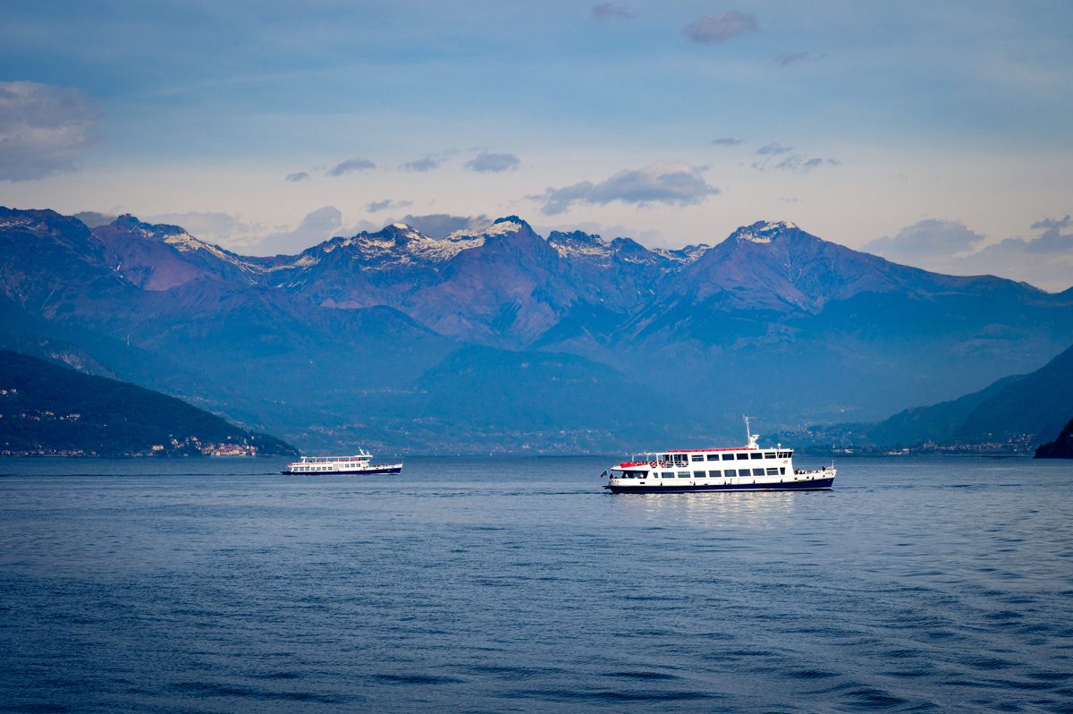 Passenger ferries cross the deep blue waters of Lake Como beneath the dramatic peaks of the Italian Alps. The layered mountains, calm lake and passing boats capture the classic scenery and everyday rhythm of northern Italy.