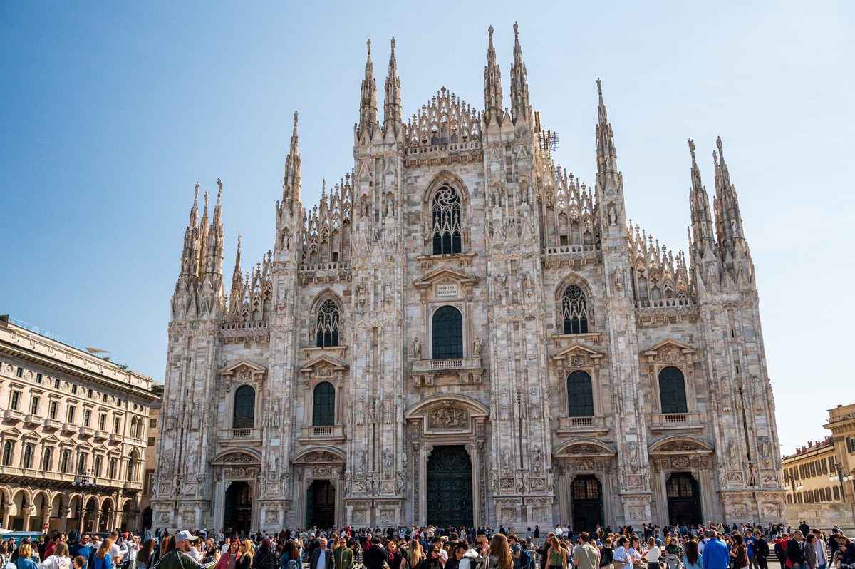 The elaborate marble façade of Milan Cathedral rises above the crowds gathered in Piazza del Duomo on a bright spring day. Gothic spires, sculpted details and clear blue skies capture one of the most iconic sights in the heart of Milan.