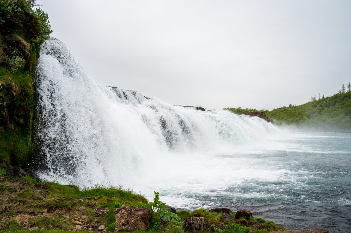An intimate, close-up perspective of a powerful waterfall, capturing the forceful surge of glacial water as it spills over the rocky drop and churns into mist.